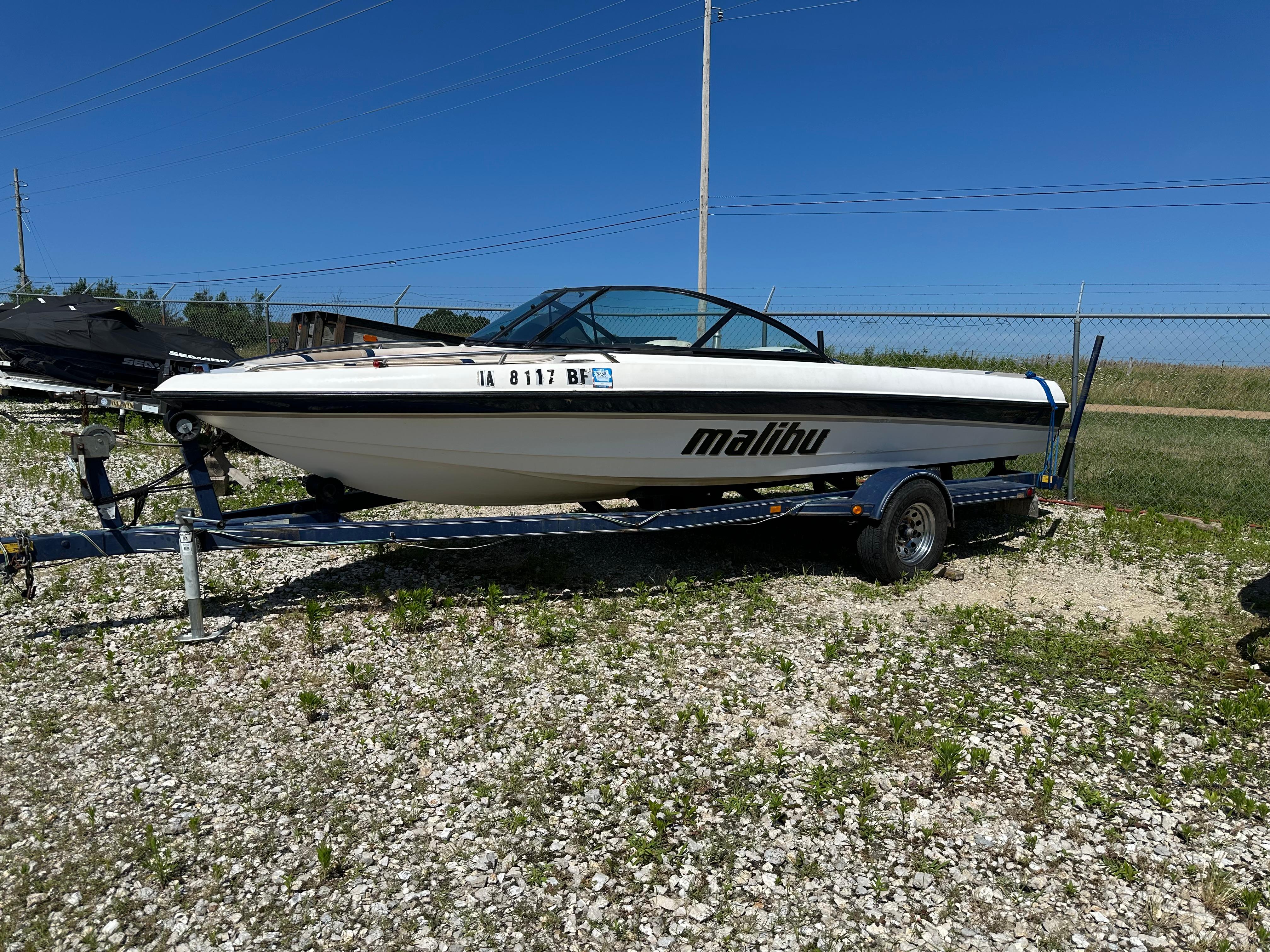 Malibu 20 Response LX 1999 Malibu 20 Response LX boat on trailer, parked on gravel lot under clear blue sky.