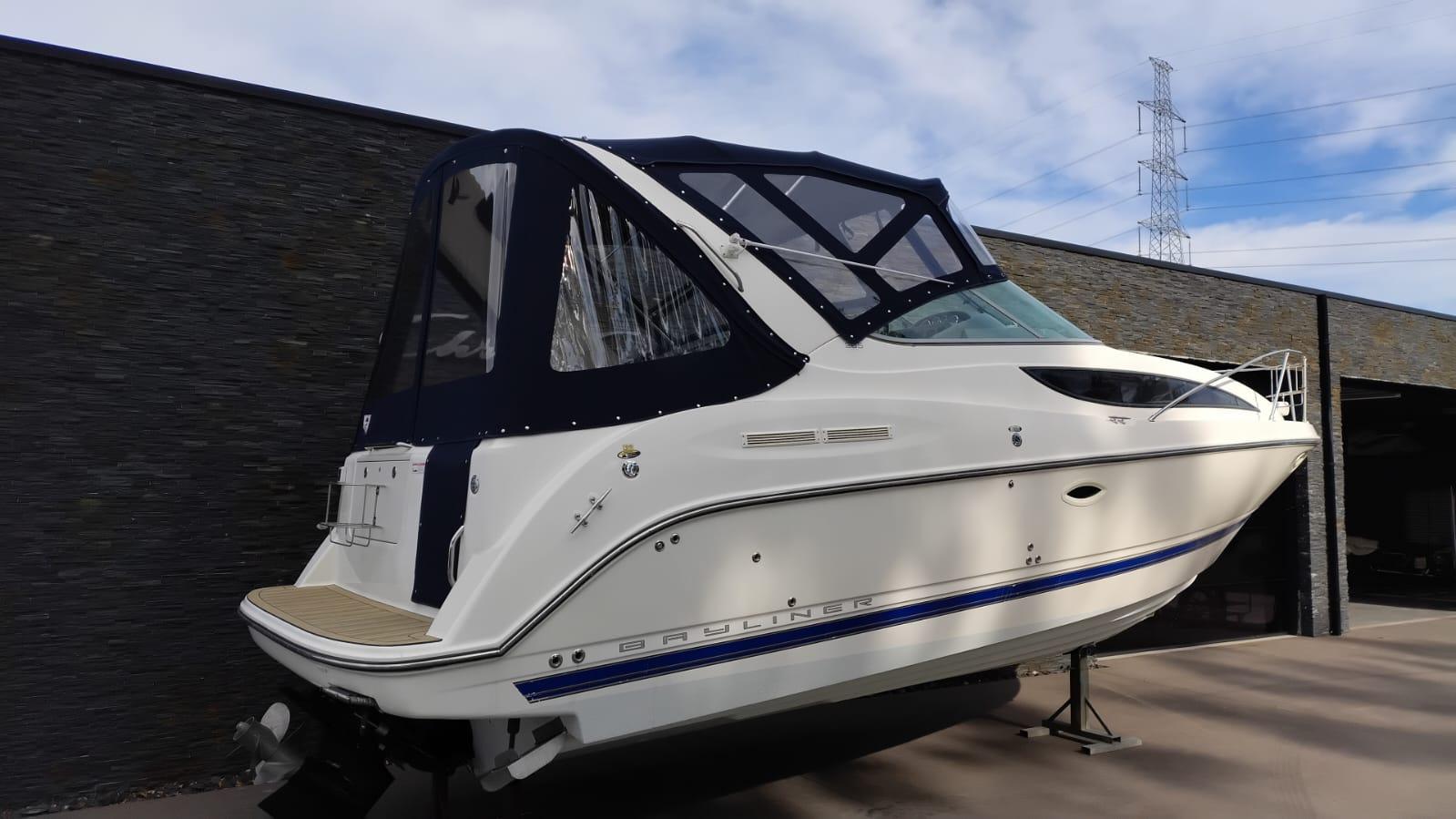 Bayliner 285 2008 Bayliner 285 boat with blue canopy, displayed outdoors against a stone wall.