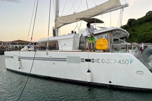 Lagoon 450 F 2015 Lagoon 450 F catamaran docked, person on deck, scenic marina backdrop.