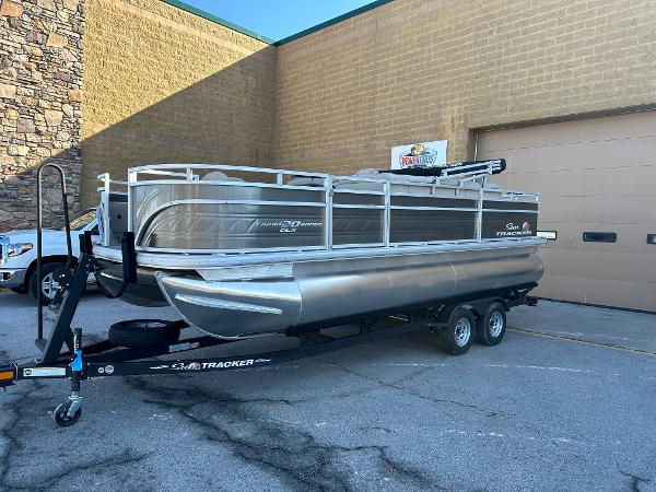 Sun Tracker Fishin' Barge 20 DLX 2024 Sun Tracker Fishin' Barge 20 DLX pontoon boat on trailer outside a building.