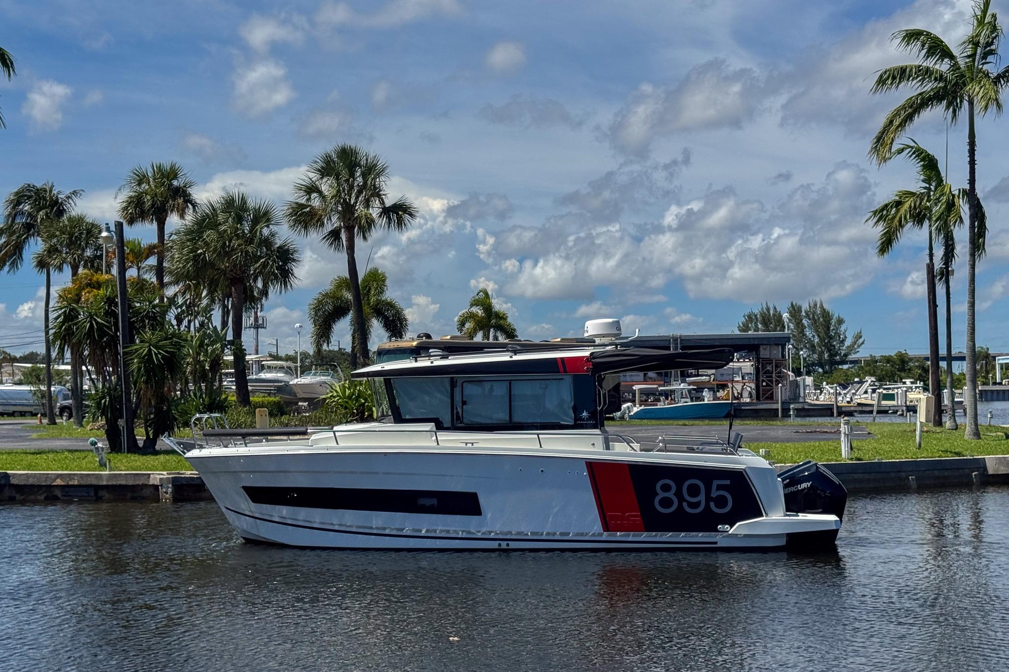 Jeanneau NC895 Sport 2023 Jeanneau NC895 Sport boat docked by palm trees under a blue sky.