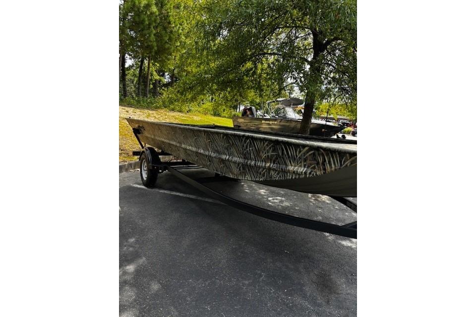 Tracker Grizzly 1860 Utility 2025 Tracker Grizzly 1860 Utility boat on trailer, parked outdoors under trees.