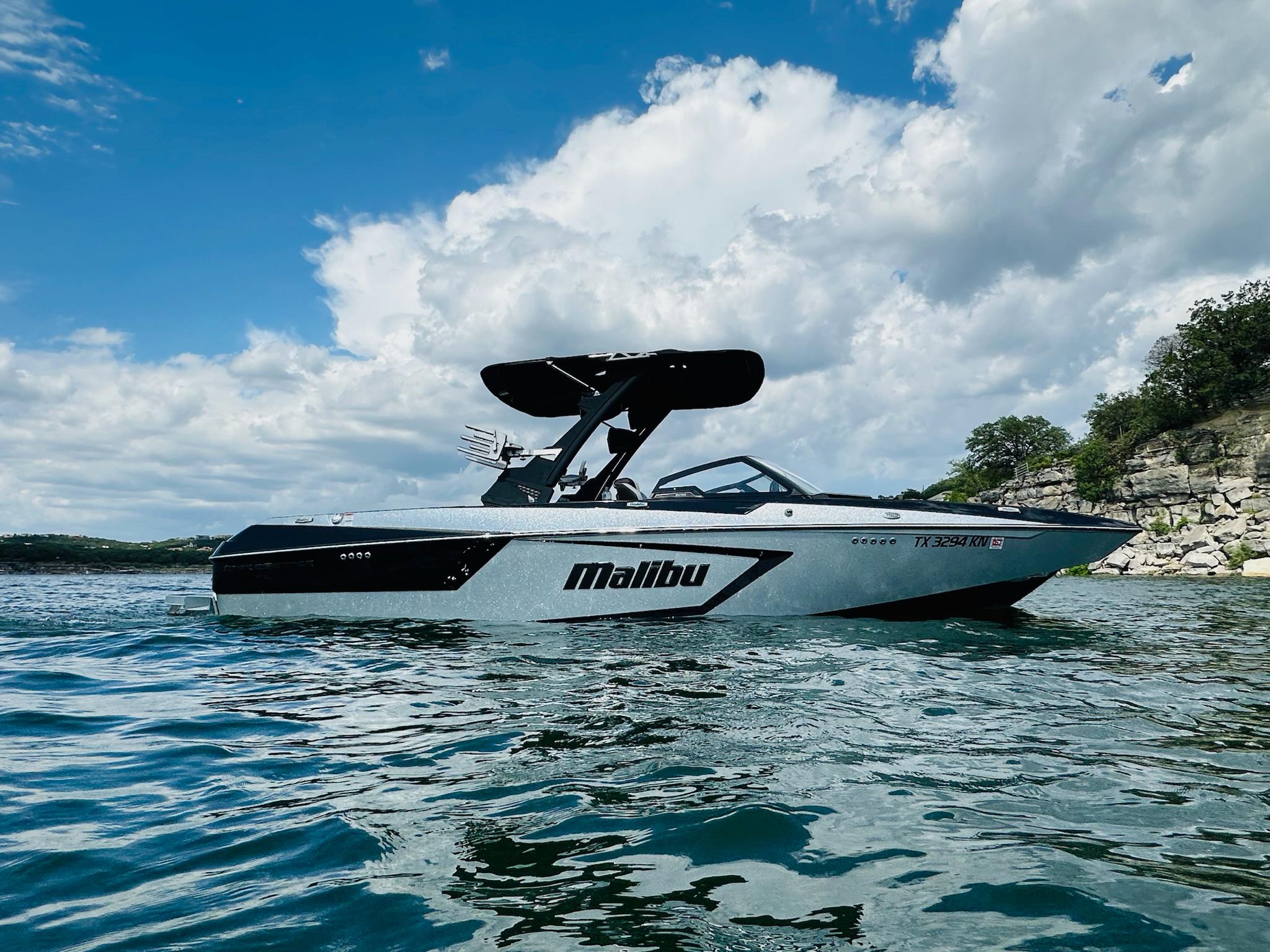 Malibu Wakesetter 24 MXZ 2022 Malibu Wakesetter 24 MXZ boat on a scenic lake under a cloudy sky.
