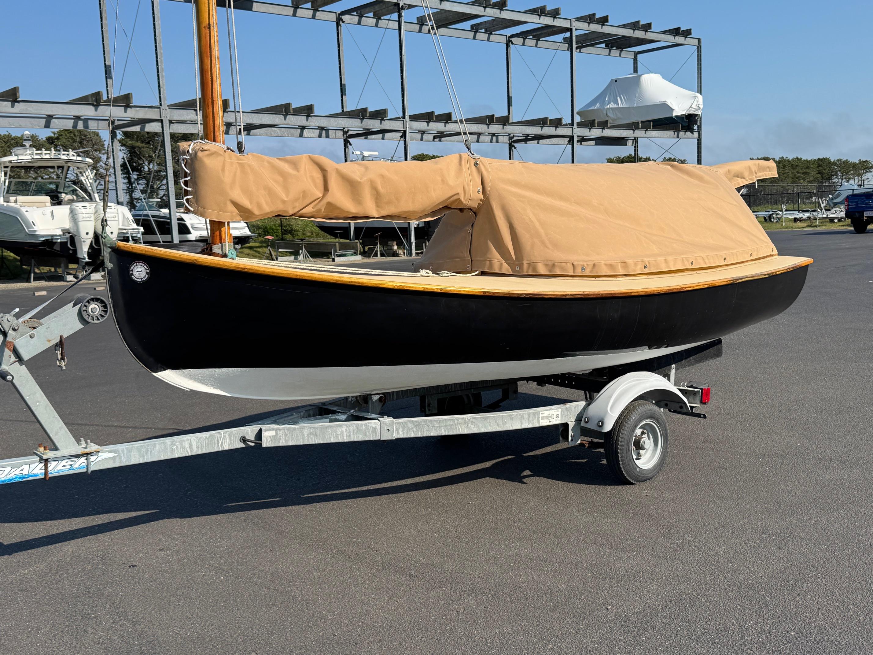 Custom Barnstable Cat Boat 2004 Custom Barnstable Cat Boat on trailer with tan cover in marina setting.