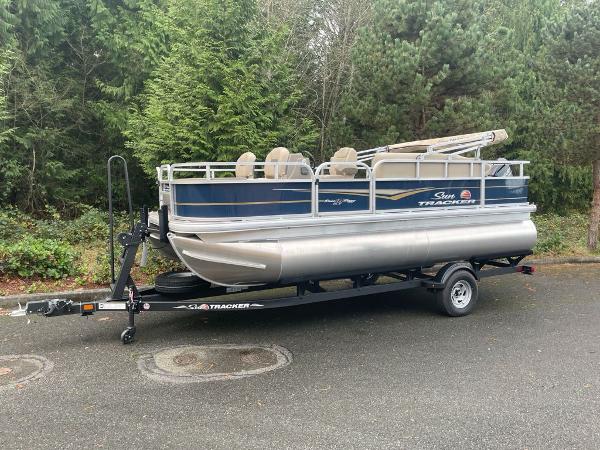Sun Tracker Bass Buggy 18 DLX 2025 Sun Tracker Bass Buggy 18 DLX pontoon boat on trailer, parked near lush greenery.