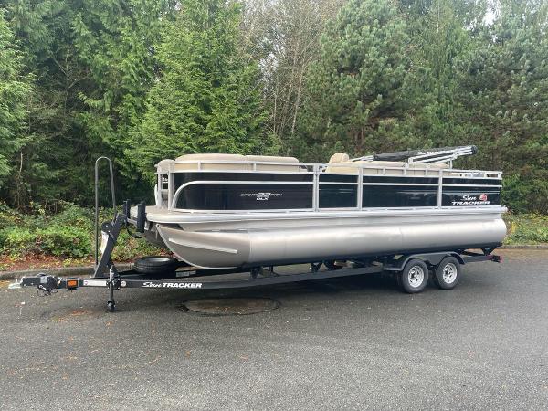 Sun Tracker SportFish 22 DLX 2025 Sun Tracker SportFish 22 DLX pontoon boat on trailer, parked near lush greenery.