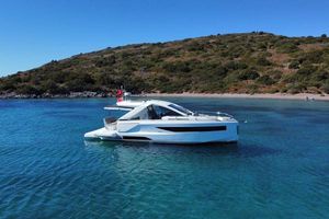 Jeanneau DB37 2024 Jeanneau DB37 yacht anchored in clear blue water near a scenic coastline.