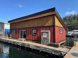 Custom 1 bed 2 bath Floating house with red siding, wooden accents, docked on water, sunny day.