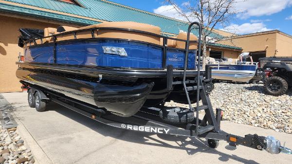 Regency 250 LE3 2025 Regency 250 LE3 pontoon boat on trailer, blue and black design, parked outdoors.