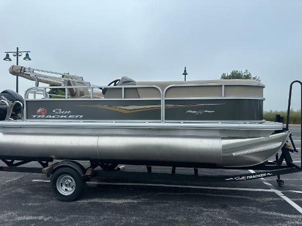 Sun Tracker Party Barge 18 DLX 2025 Sun Tracker Party Barge 18 DLX pontoon boat on trailer in parking lot.