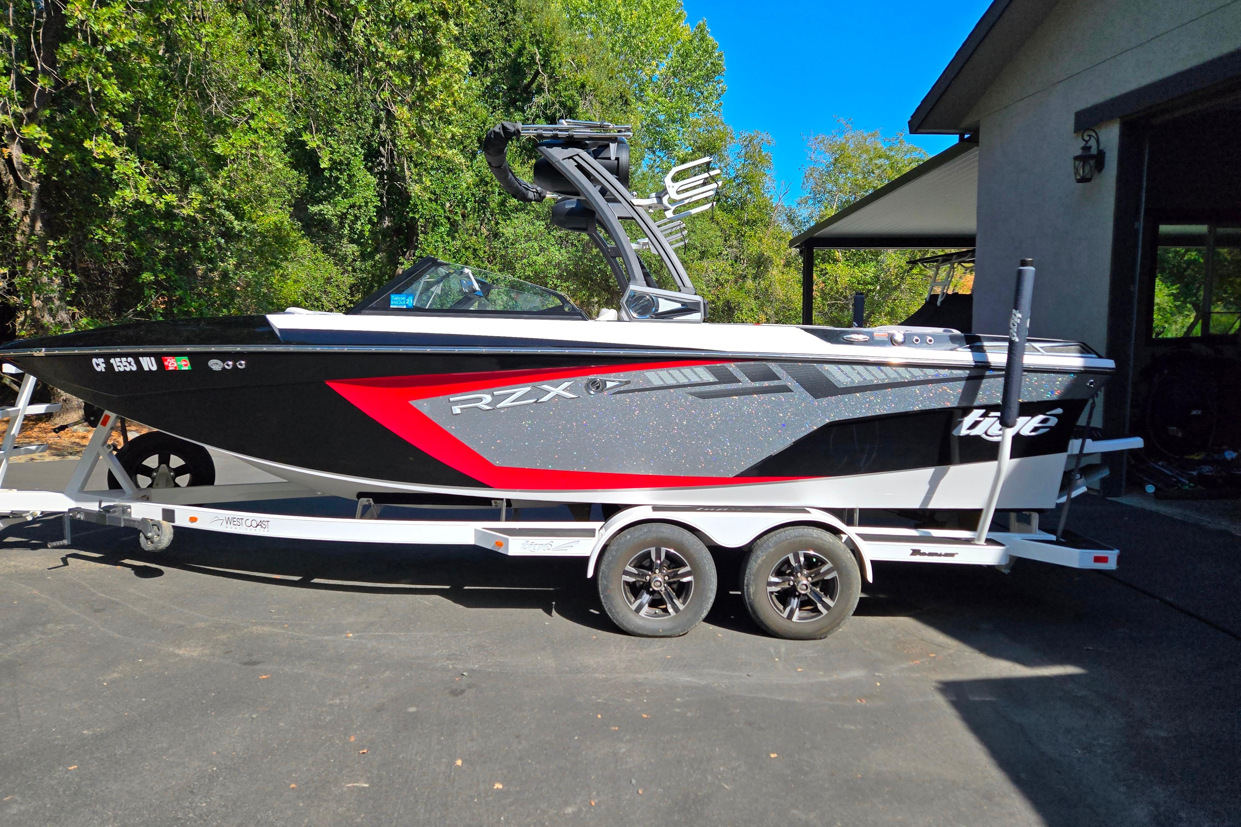 Tigé 22RZX 2021 Tigé 22RZX boat on trailer, parked outdoors with lush greenery background.