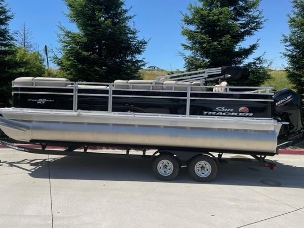 Sun Tracker SportFish 22 DLX 2025 Sun Tracker SportFish 22 DLX pontoon boat on trailer, parked outdoors.
