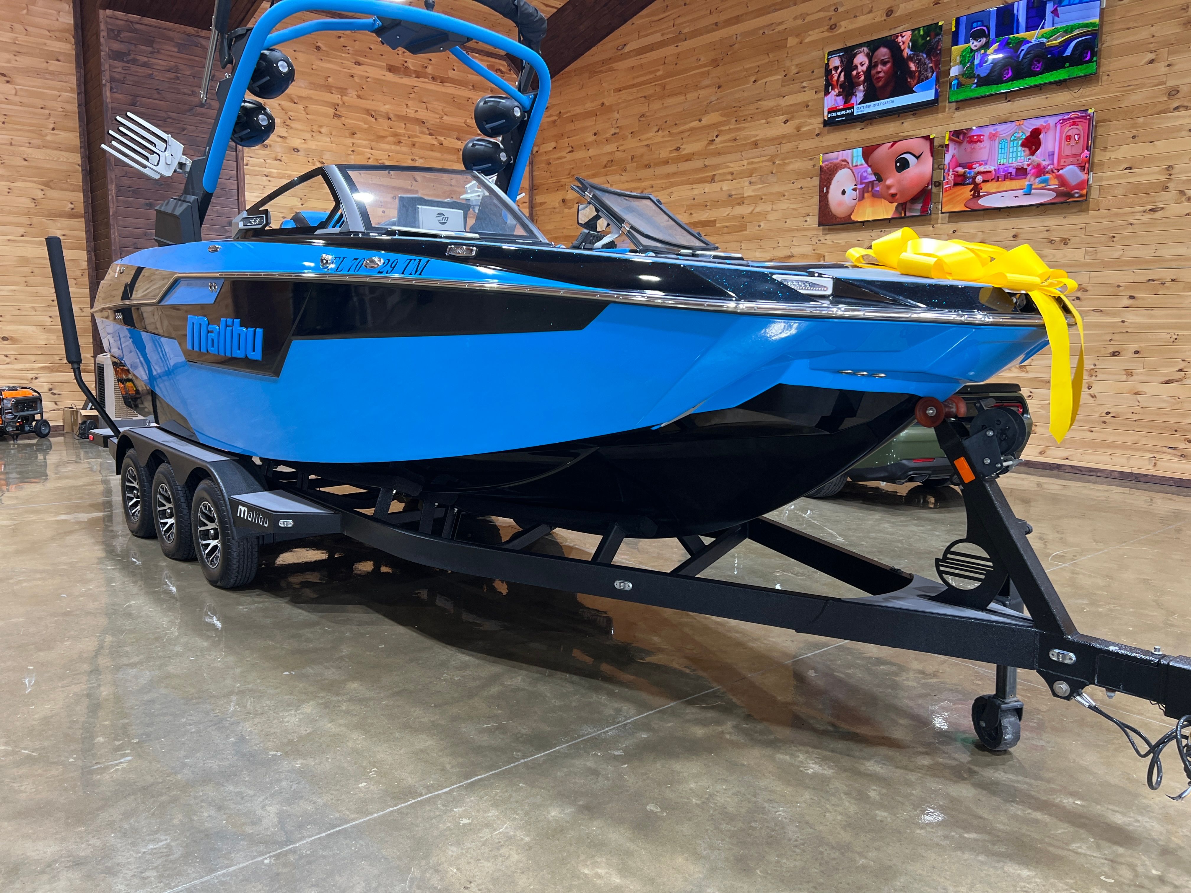 Malibu M240 2022 Malibu M240 boat in showroom, blue and black design, on trailer with yellow bow.