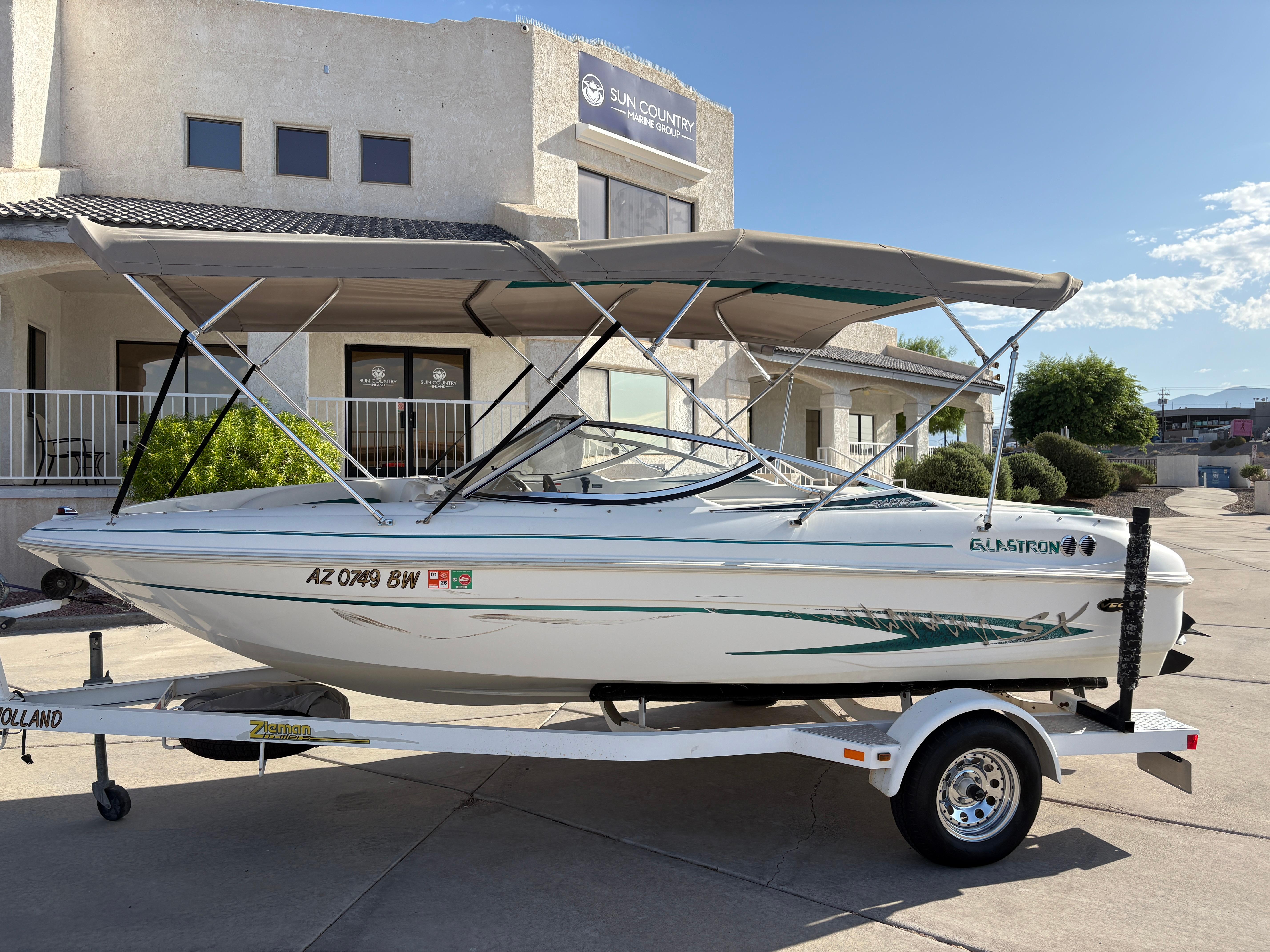 Glastron SX 175 2003 Glastron SX 175 boat on trailer with canopy, parked outside a building.