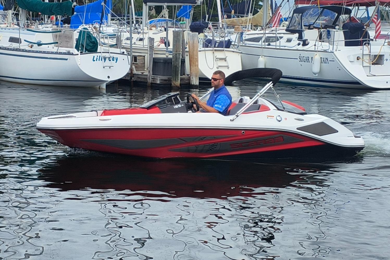 Scarab 165 LX 2025 Scarab 165 LX boat cruising in a marina with sailboats in the background.