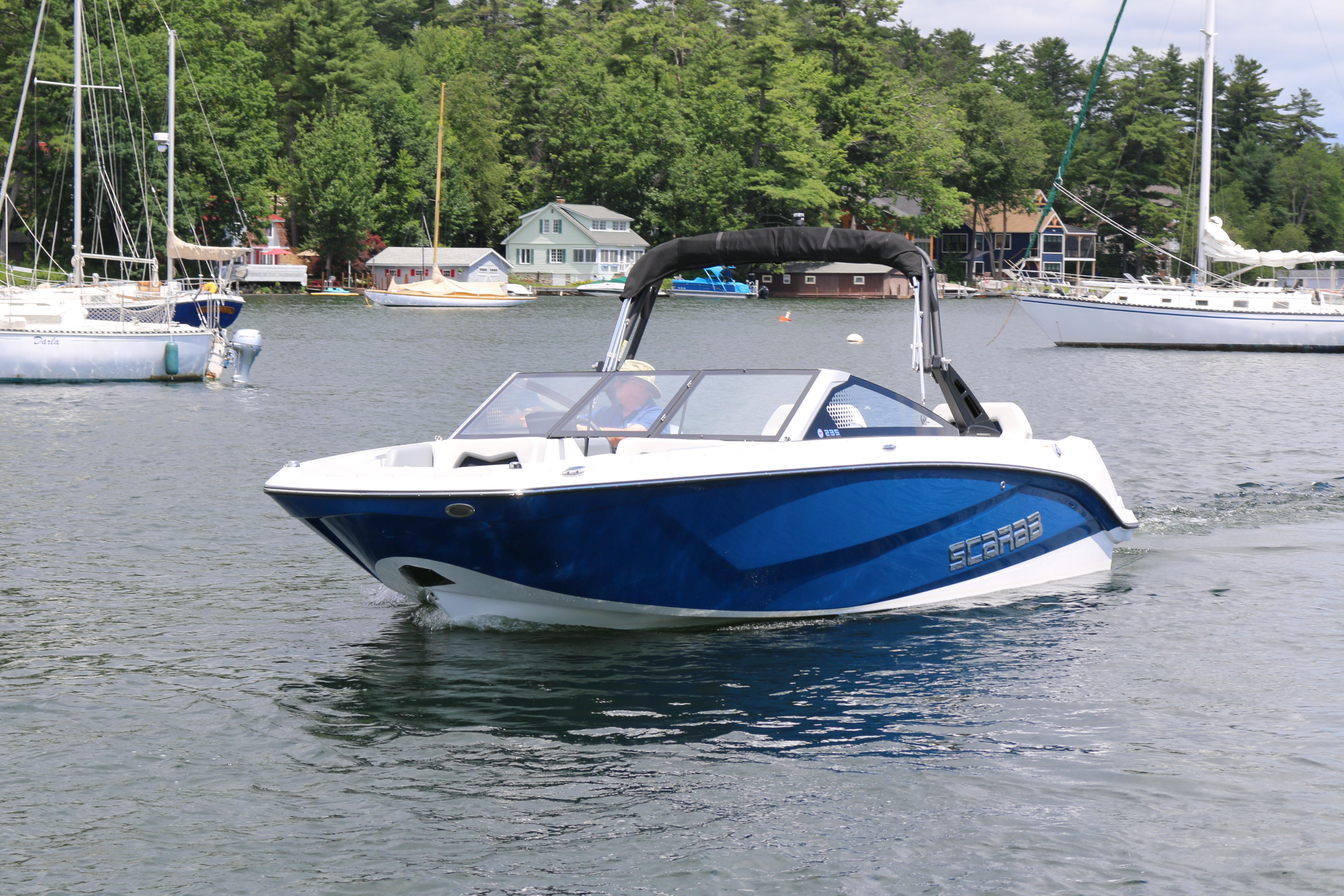 Scarab 235 SE 2025 Scarab 235 SE boat cruising on a scenic lake with surrounding sailboats.