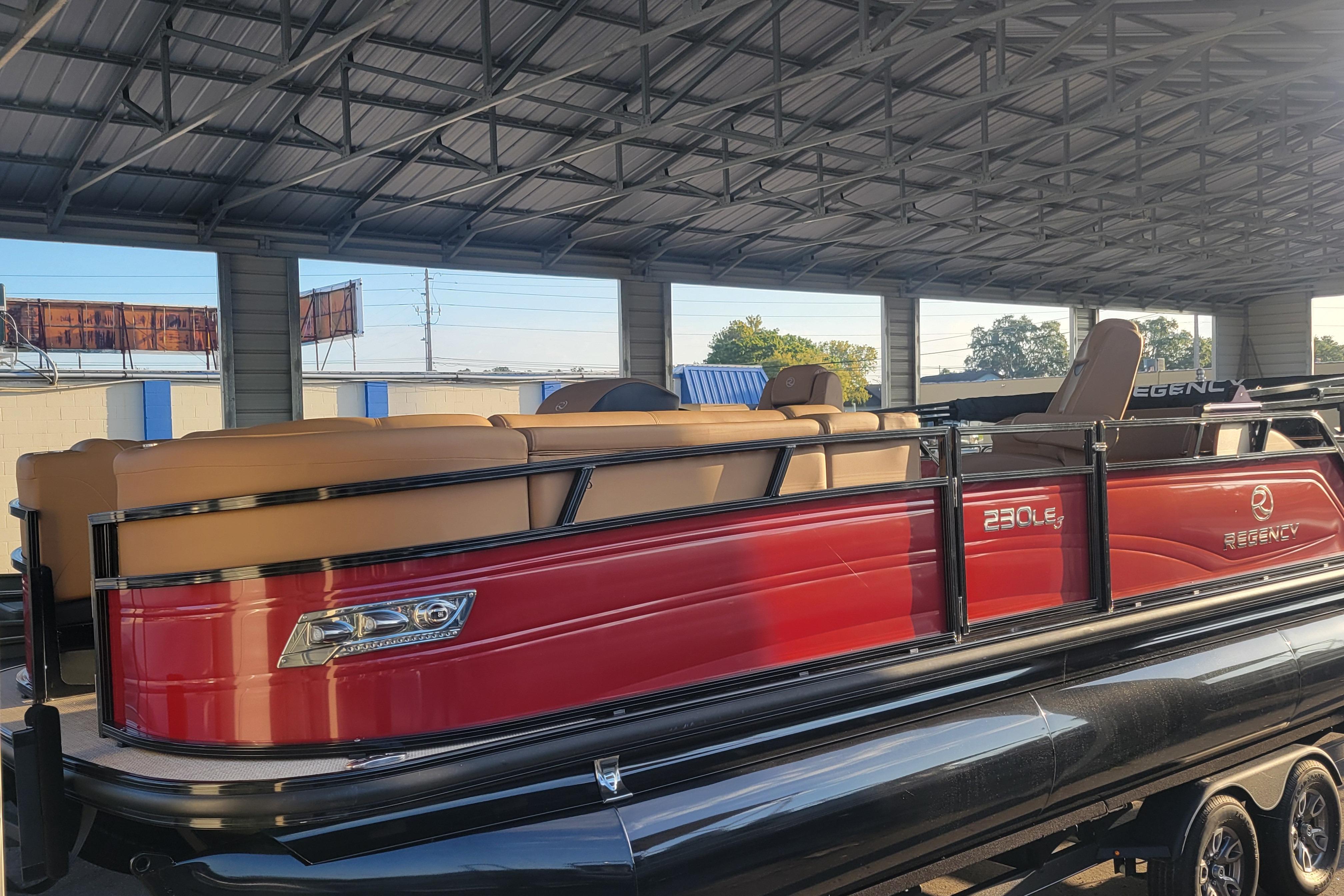 Regency 230 LE3 Sport 2024 Regency 230 LE3 Sport pontoon boat with red exterior under a metal roof.