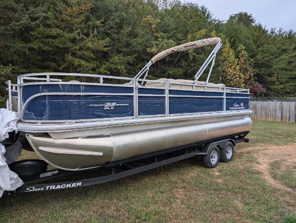 Sun Tracker Fishin' Barge 22 DLX 2025 Sun Tracker Fishin' Barge 22 DLX pontoon boat on trailer, parked on grass.