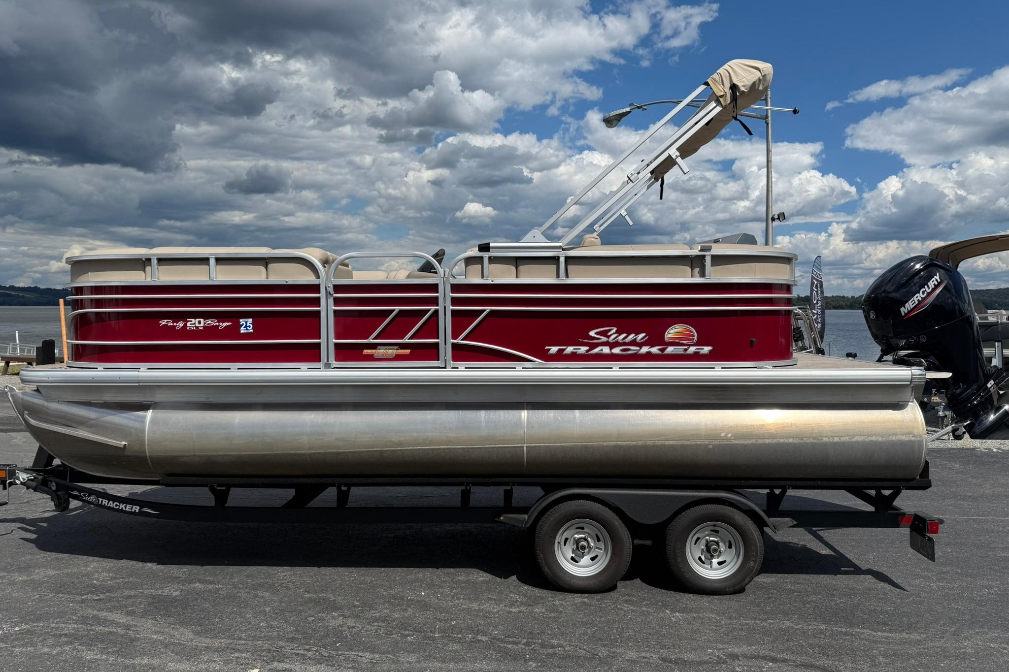 Sun Tracker Party Barge 20 DLX 2023 Sun Tracker Party Barge 20 DLX pontoon boat on trailer, under cloudy sky.