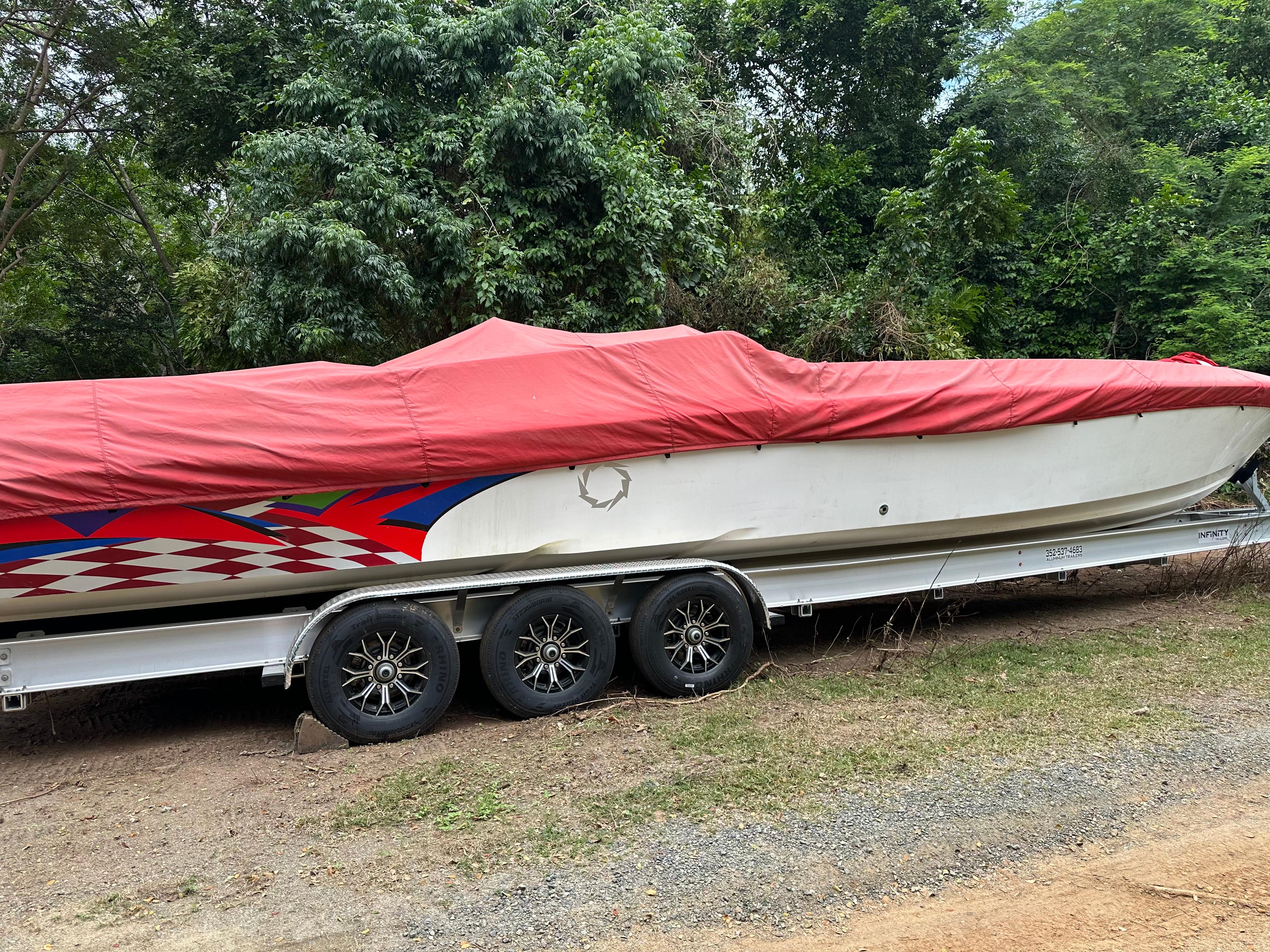 Fountain Lightning 1997 Fountain Lightning boat with red cover on trailer, surrounded by lush greenery.