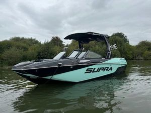 Supra SV 2024 Supra SV boat on calm water with lush greenery background.