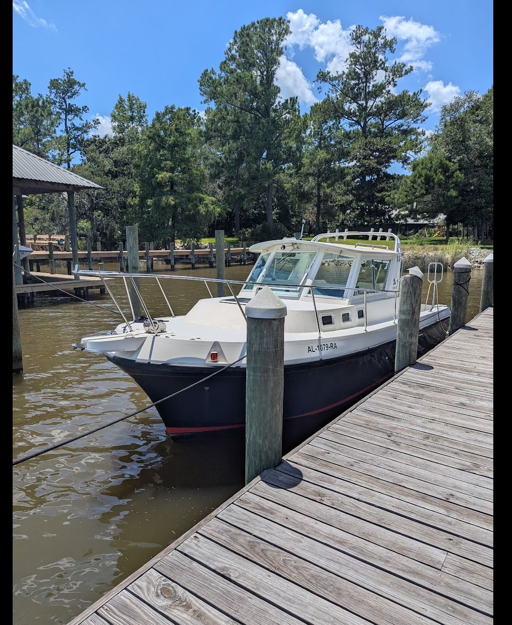 Albin 28 1999 Albin 28' boat docked by a wooden pier, surrounded by trees and calm water.