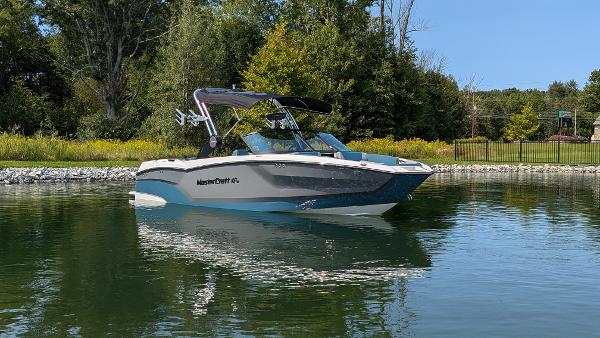 MasterCraft NXT23 2025 MasterCraft NXT23 boat on a calm lake, surrounded by lush greenery.