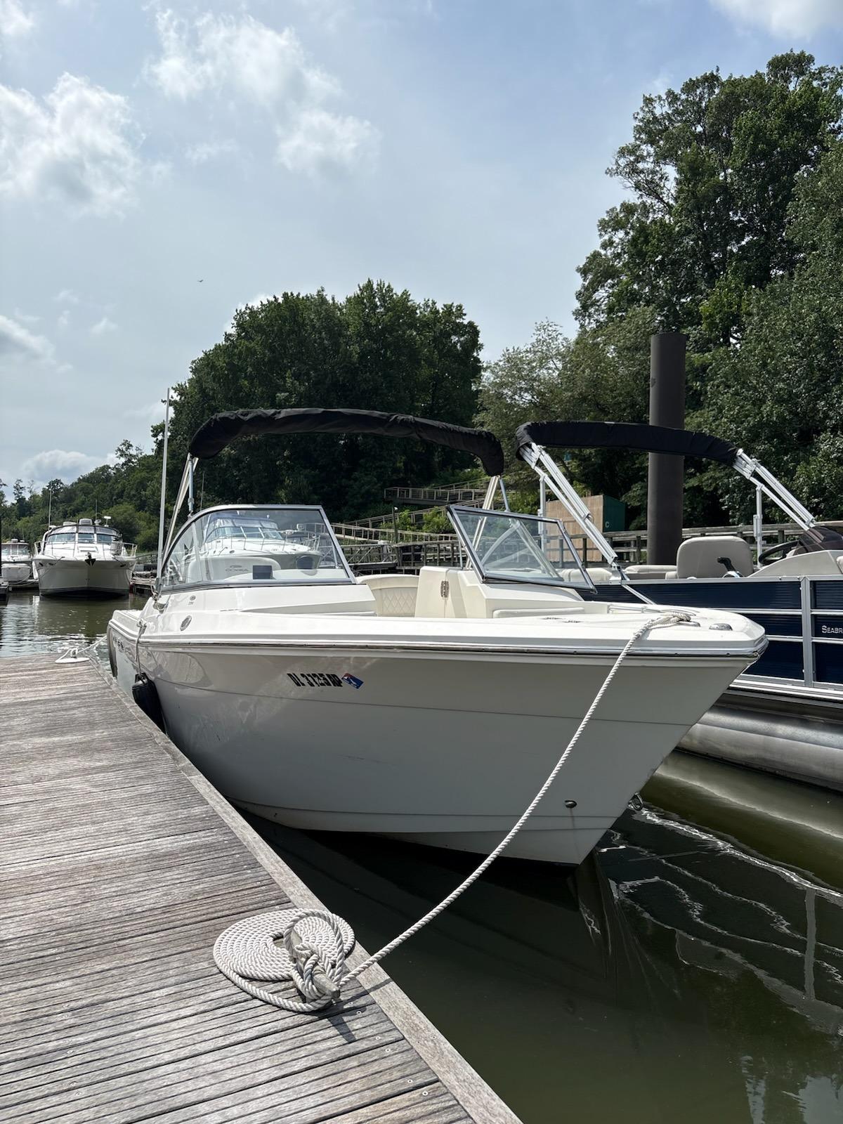 Cobia 220 Dual Console 2023 Cobia 220 Dual Console boat docked at marina, sunny day, lush trees in background.