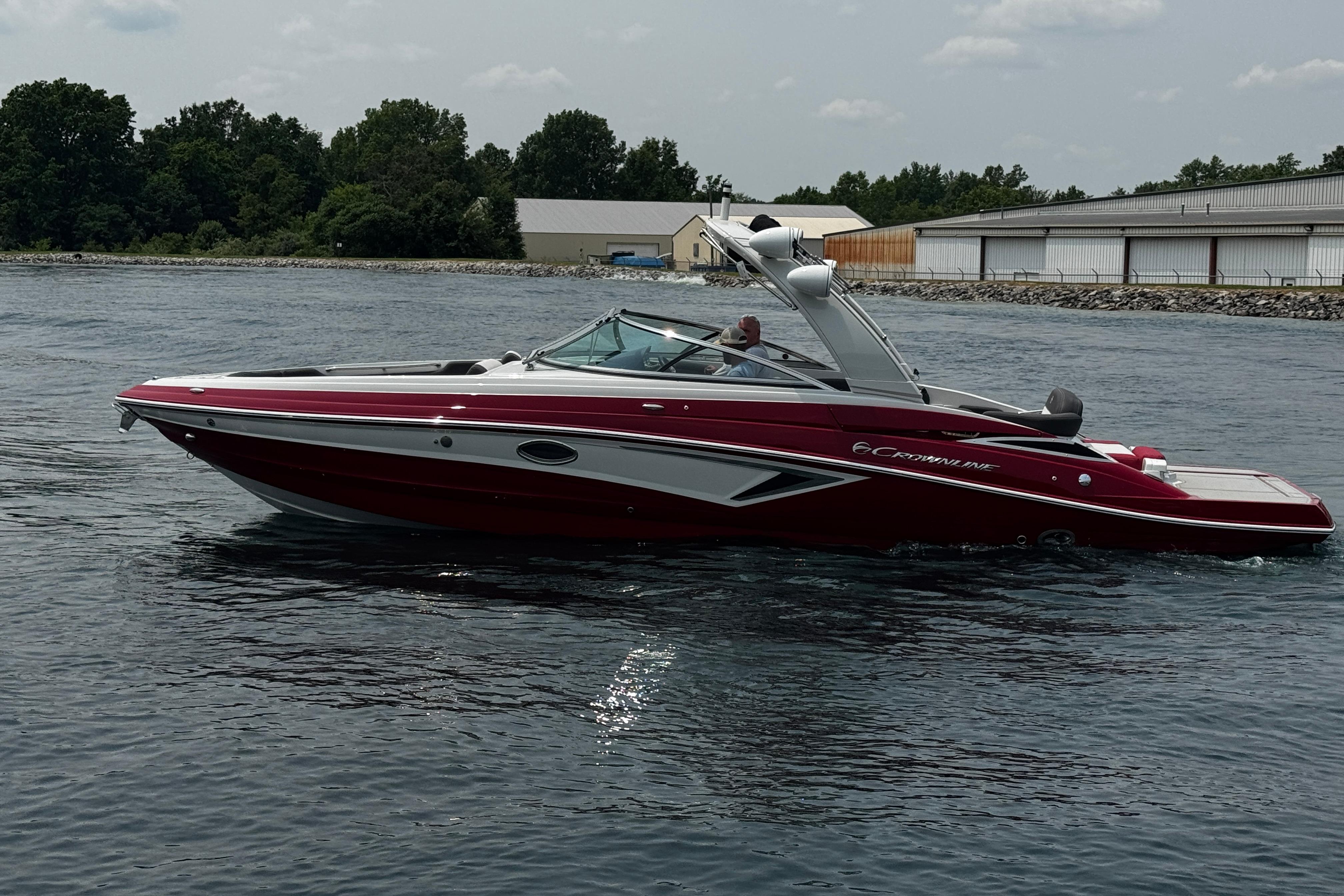 Crownline 298 SS 2026 Crownline 298 SS boat cruising on a calm lake near a marina.