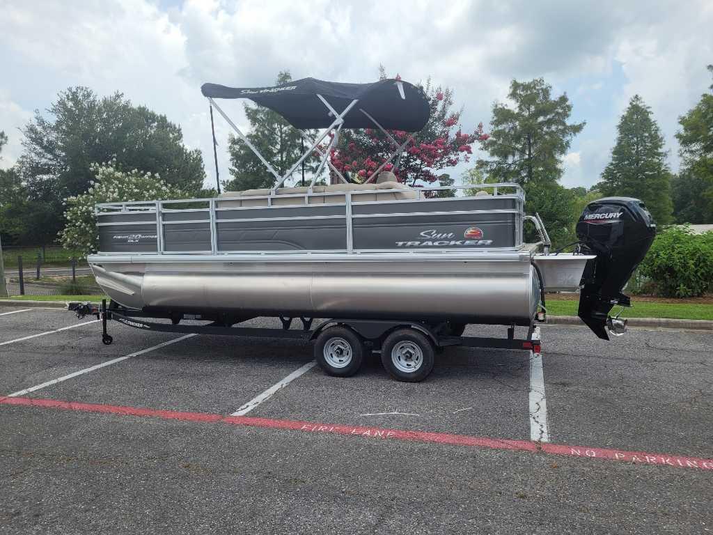 Sun Tracker Fishin' Barge 20 DLX 2025 Sun Tracker Fishin' Barge 20 DLX pontoon boat on trailer in parking lot.