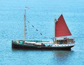 Custom Gronigen Vintage 1930 Custom Gronigen sailboat with red sail on calm blue sea.