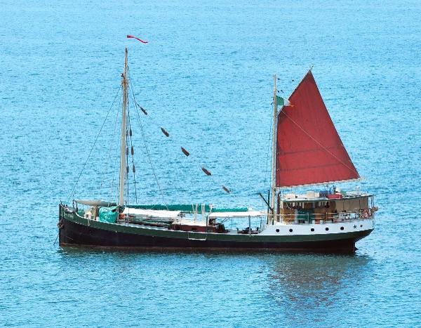 Custom Gronigen Vintage 1930 Custom Gronigen sailboat with red sail on calm blue sea.