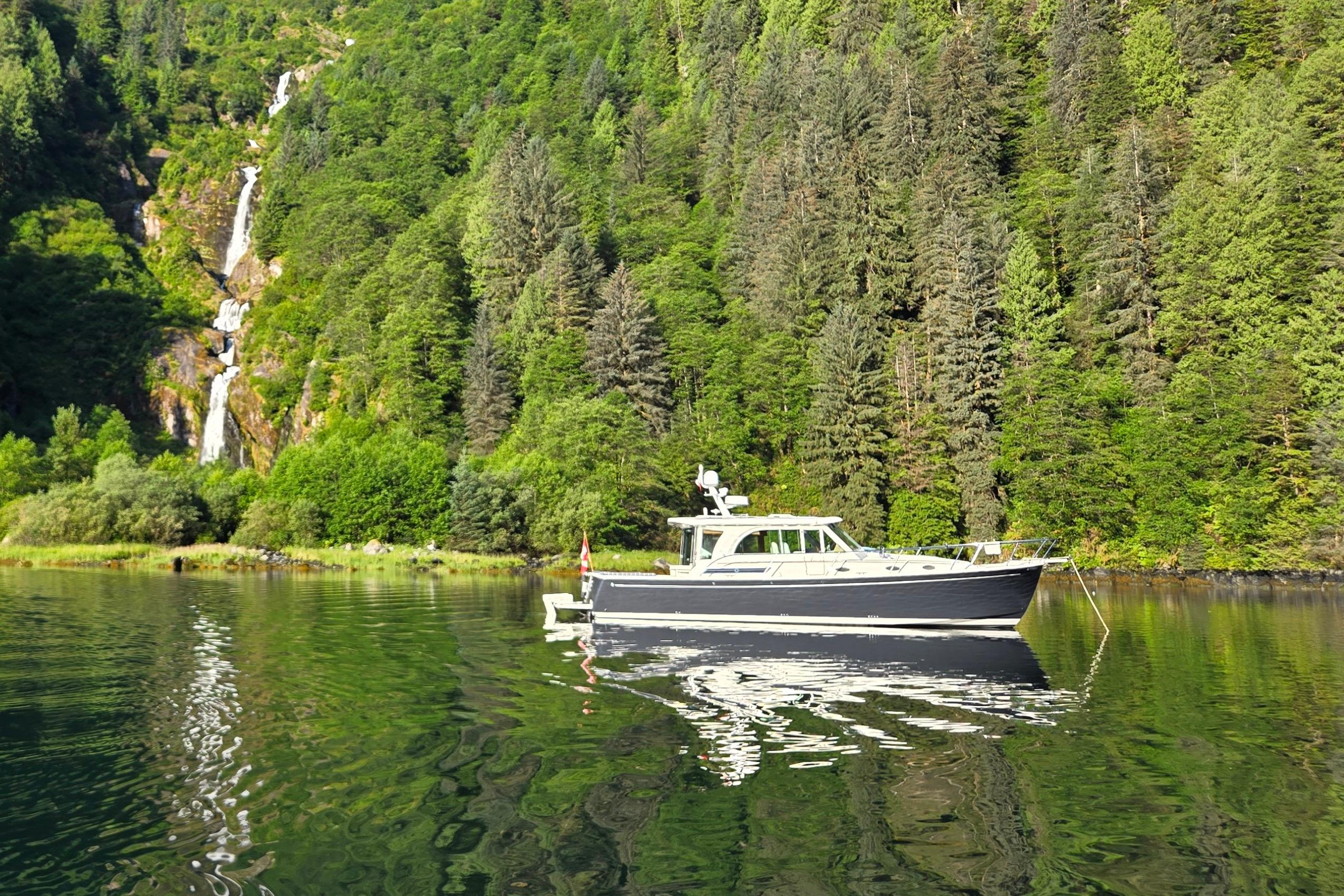 Back Cove 41 2016 Back Cove 41 yacht on serene lake with lush forest and waterfall backdrop.