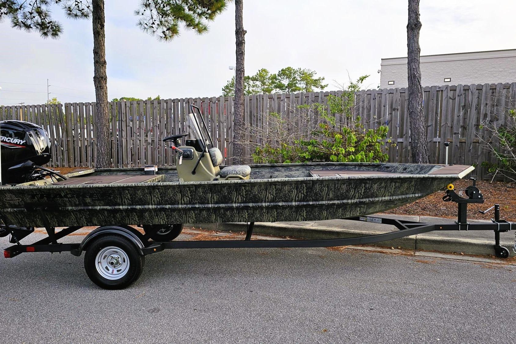 Tracker Grizzly 1860 CC 2026 Tracker Grizzly 1860 CC boat on trailer, parked near trees and fence.