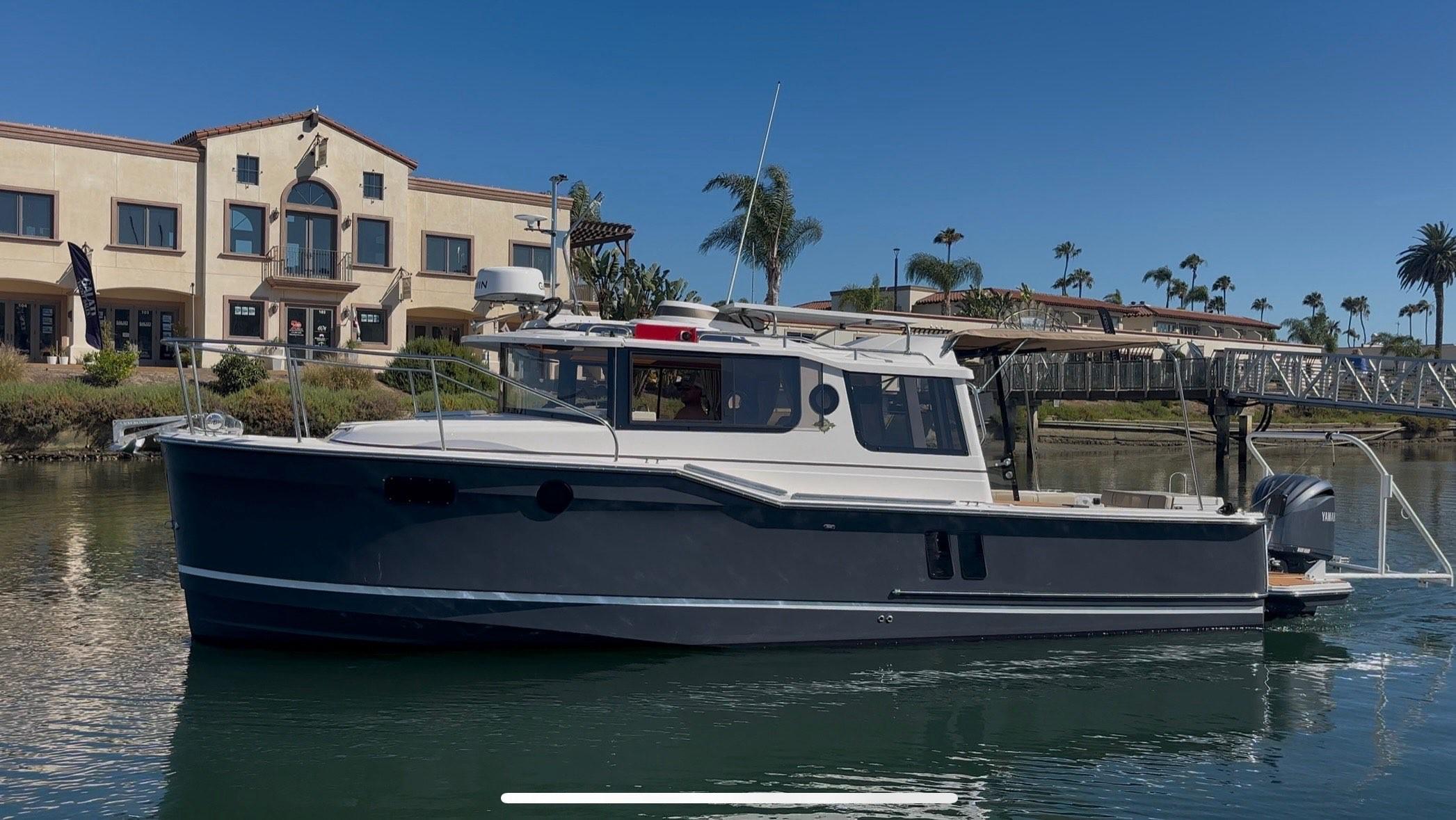 Ranger Tugs R-27 2025 Ranger Tugs R-27 boat docked near waterfront buildings and palm trees.