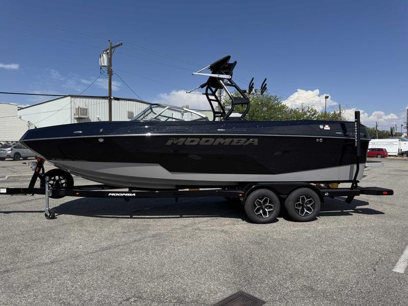 Moomba Tykon 2025 Moomba Tykon boat on trailer, parked in industrial area under clear sky.