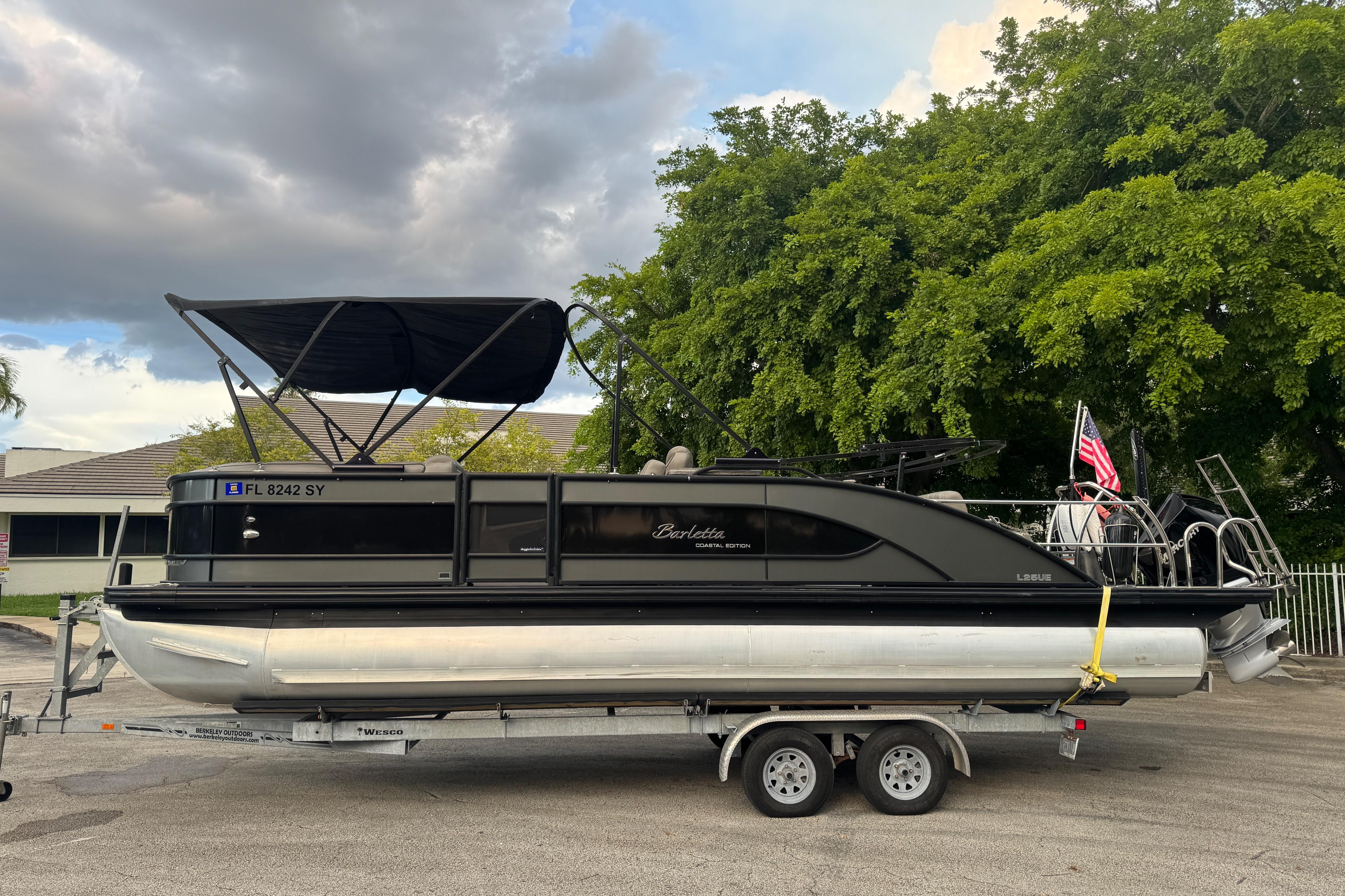 Barletta L25UE 2021 Barletta L25UE pontoon boat on trailer, parked outdoors with trees in background.