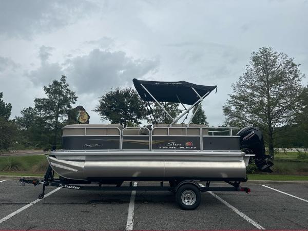 Sun Tracker Party Barge 18 DLX 2025 Sun Tracker Party Barge 18 DLX pontoon boat on trailer in parking lot.