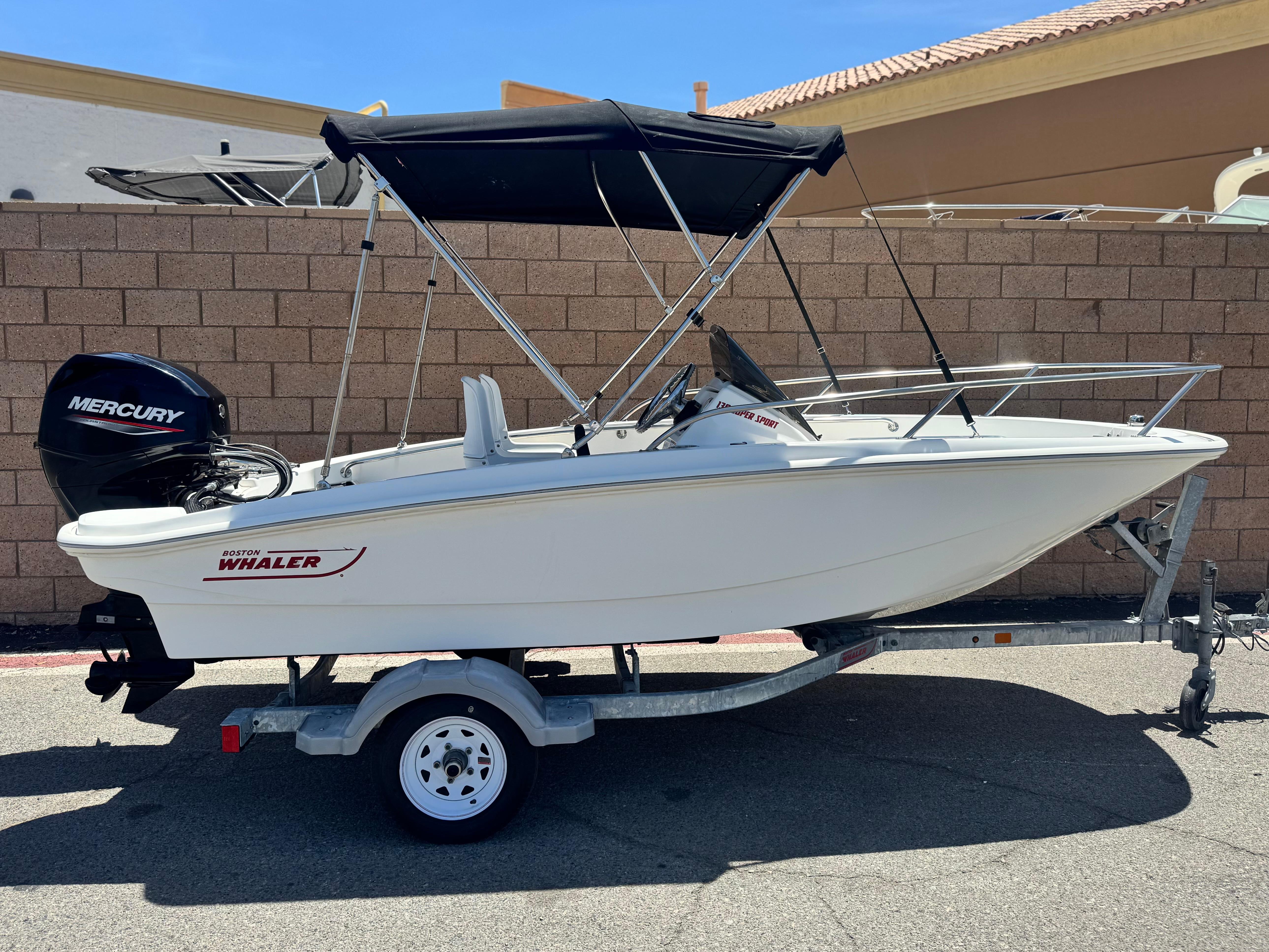 Boston Whaler 130 Super Sport 2021 Boston Whaler 130 Super Sport boat on trailer, with Mercury engine, parked outdoors.
