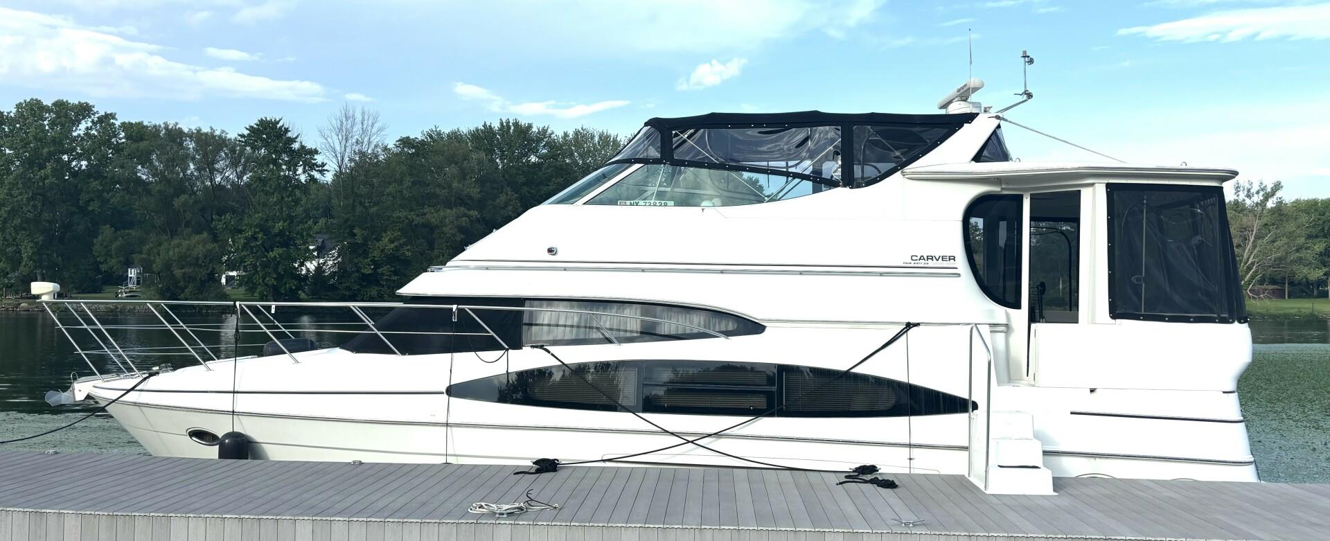 Carver 466 Motor Yacht 2004 Carver 466 Motor Yacht docked by a serene lake with lush trees.
