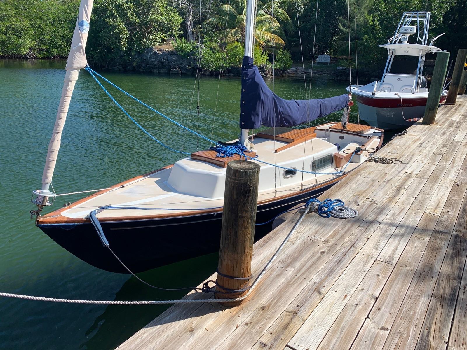 Sailboat 24 Vintage 1968 Sailboat 24 docked on a wooden pier, surrounded by lush greenery.
