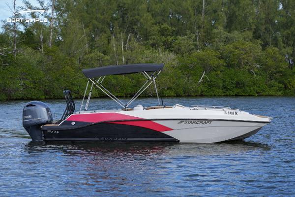 Starcraft SVX 210 2023 Starcraft SVX 210 boat on a calm lake with lush greenery.