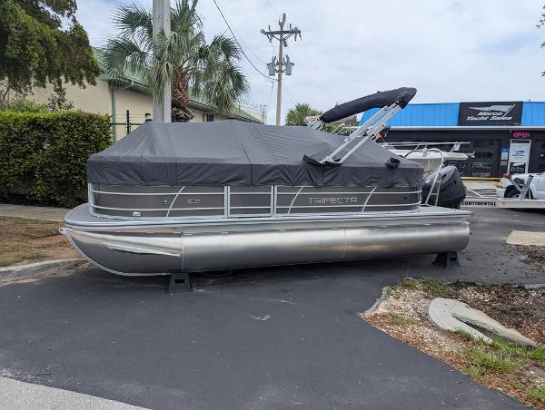 Trifecta 20RFLE 2025 Trifecta 20RFLE pontoon boat with cover, parked outdoors near a marine shop.