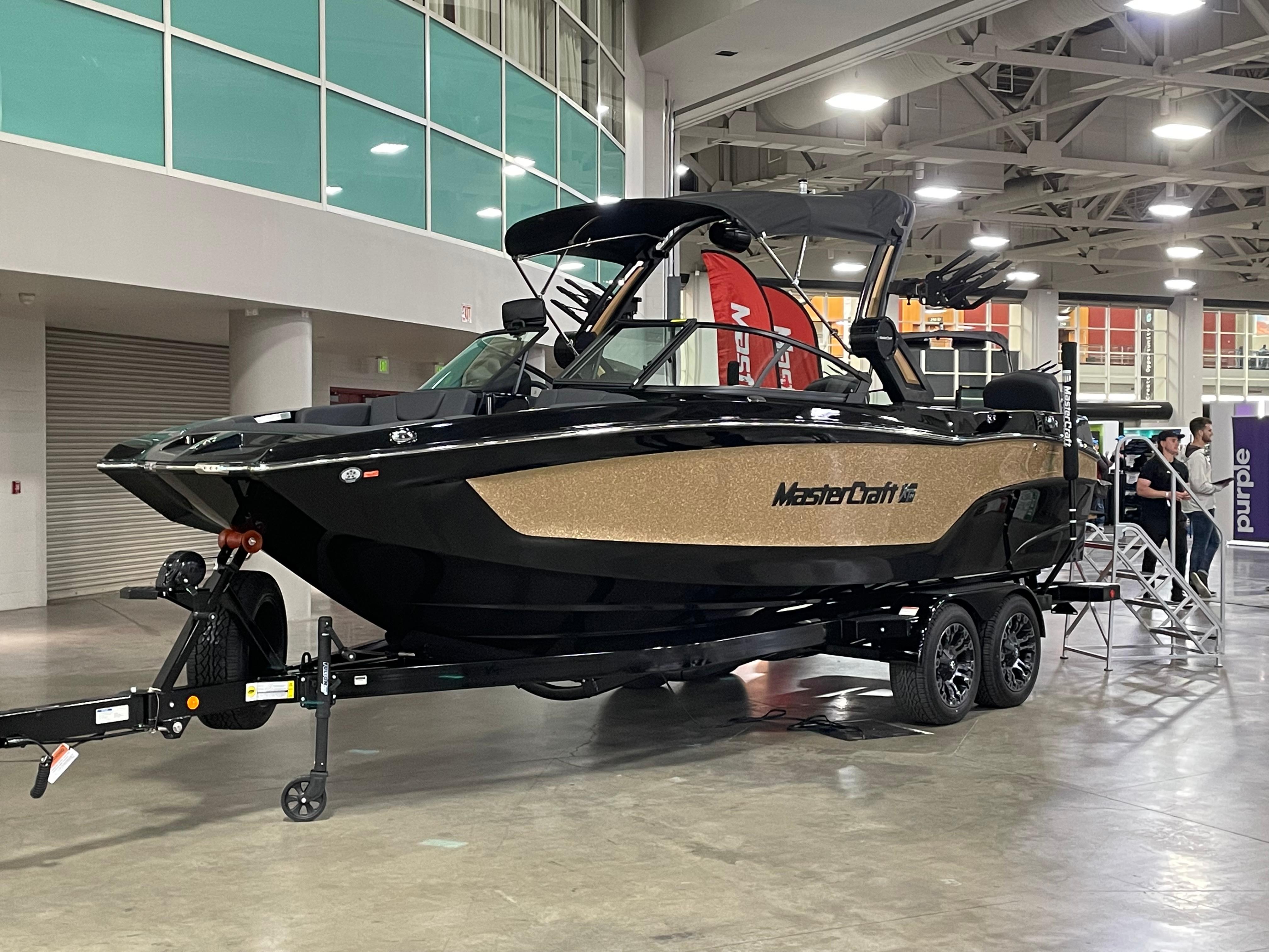 MasterCraft XT24 2022 MasterCraft XT24 boat on display indoors, black and gold design, on a trailer.