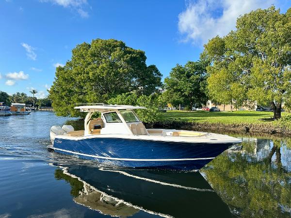 Scout 330 LXF 2025 Scout 330 LXF boat cruising on a calm river with lush green trees.
