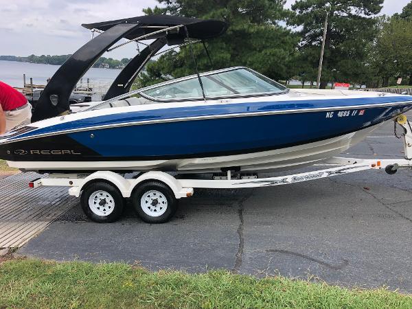 Regal 2100 2017 Regal 2100 boat on trailer, blue and white, parked near a lake.