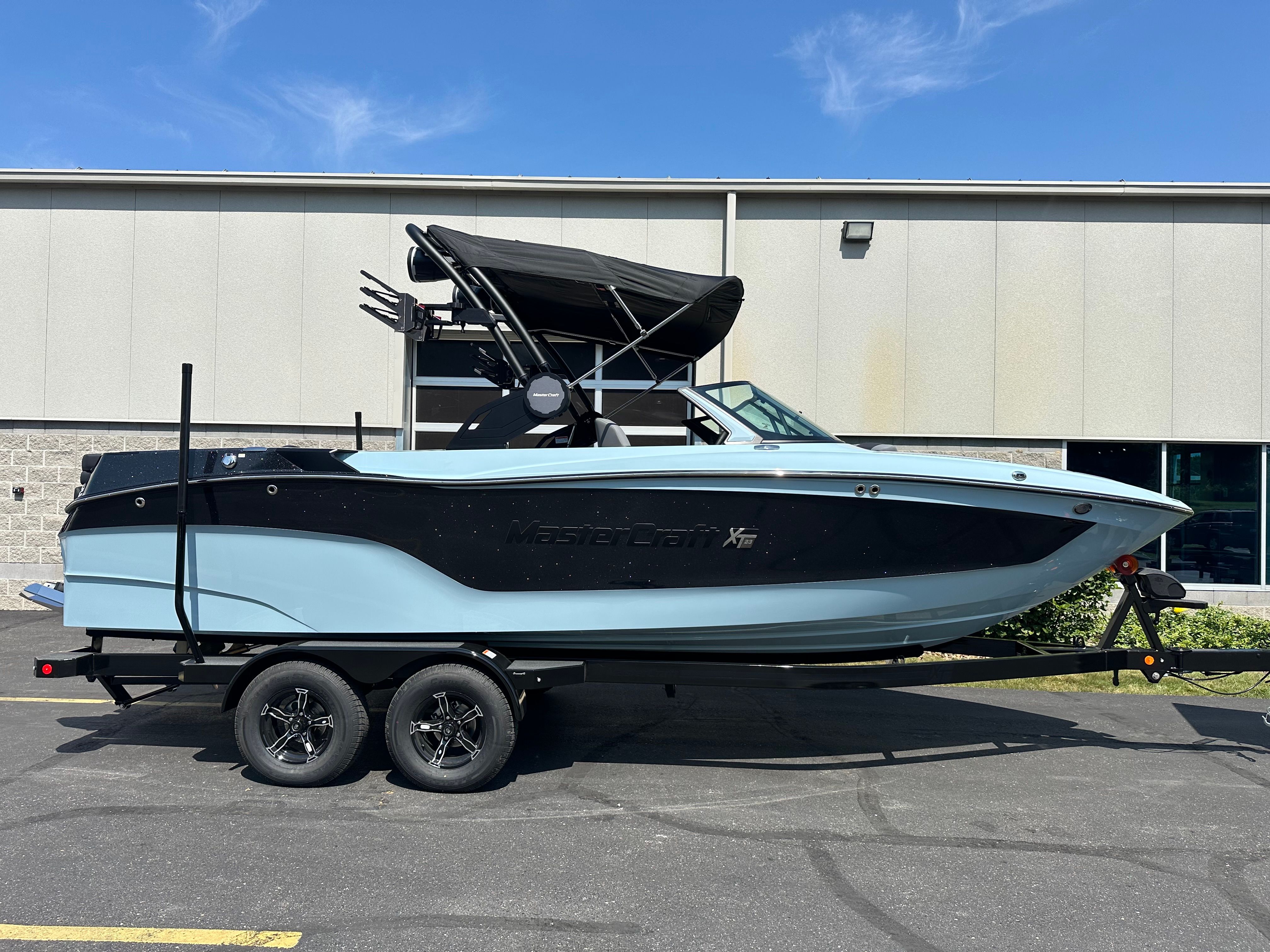 MasterCraft XT23 2025 MasterCraft XT23 boat on trailer, parked outdoors, under clear blue sky.