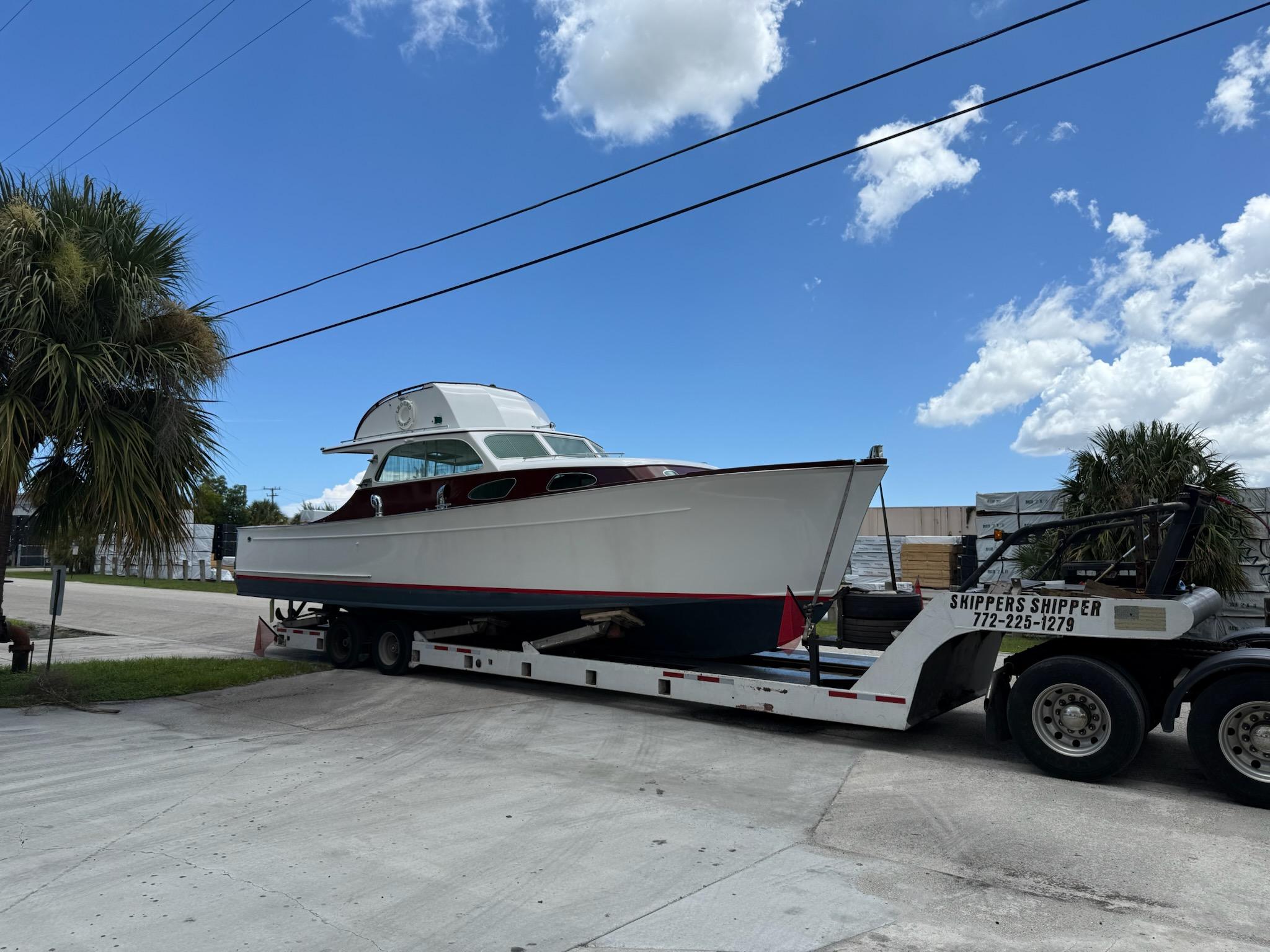 Rybovich Sport Fish 1949 Rybovich Sport Fish boat on trailer under blue sky, surrounded by palm trees.