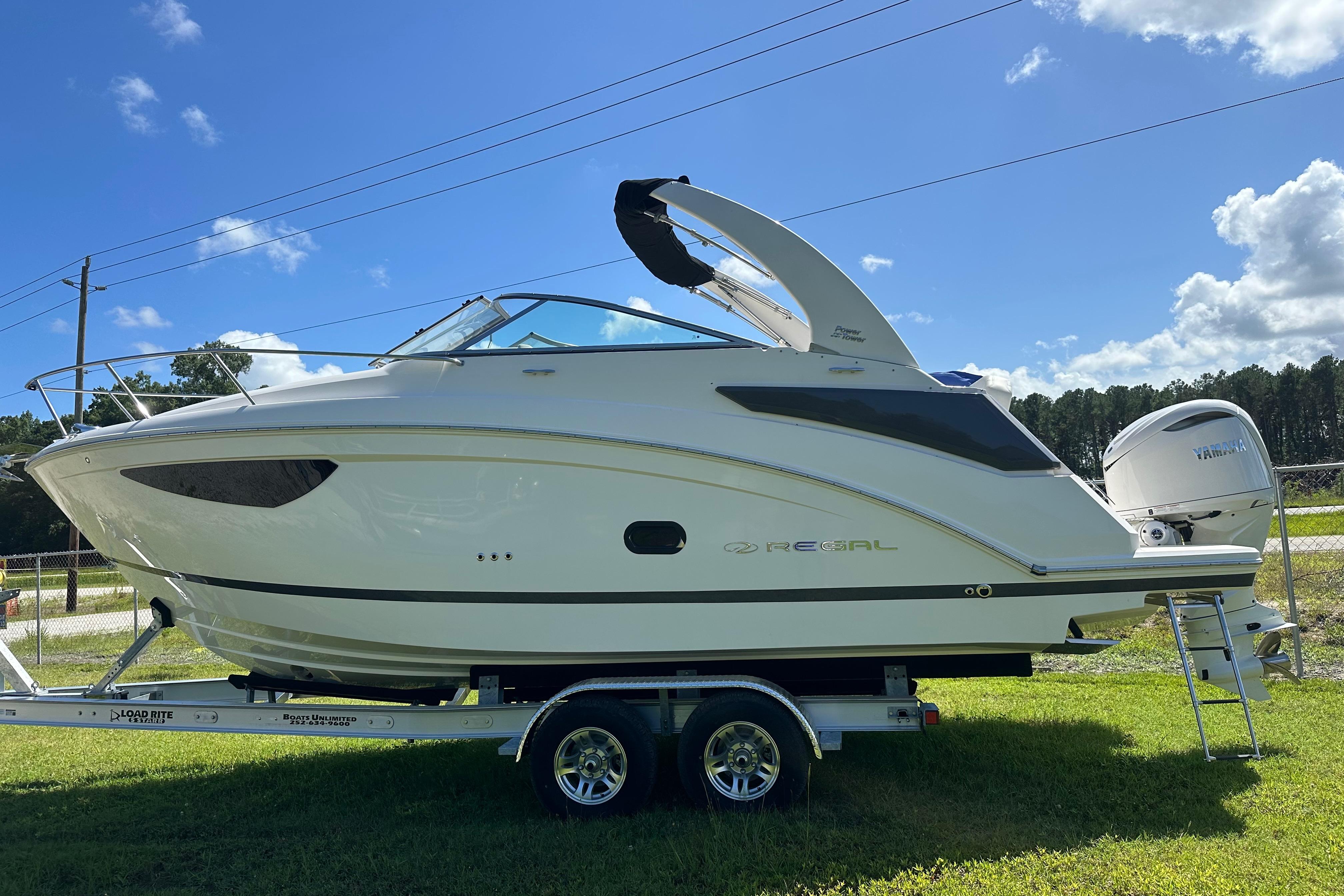 Regal 26 XO 2024 Regal 26 XO boat on trailer, parked on grass under a clear blue sky.