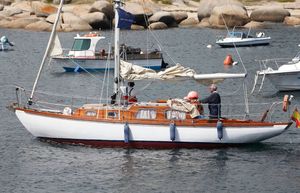 Custom One Design Vintage 1969 Custom One Design sailboat on calm water with rocky shoreline background.